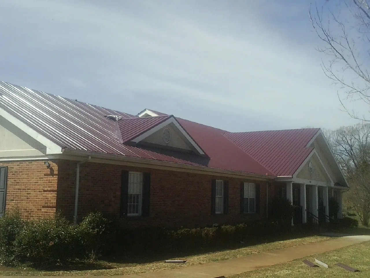 Red metal roof with gabled entries on a long brick building, from a Hail Damage Roof Repair job in Earleville